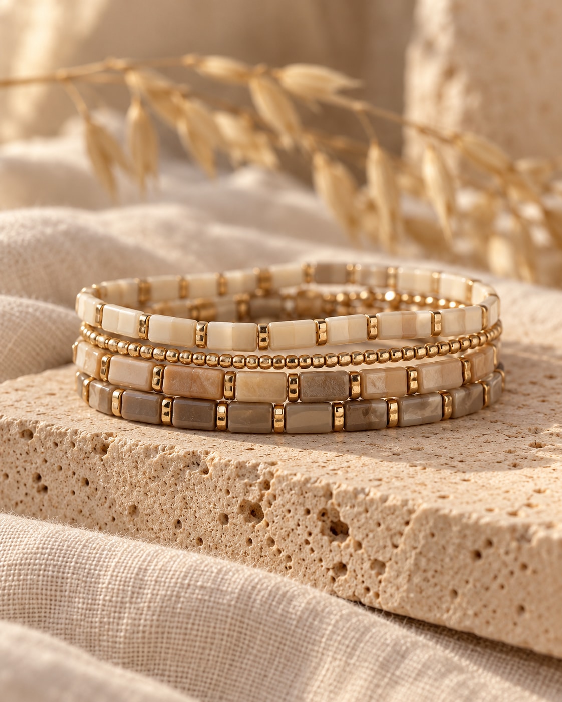 The Earth Edit study: sand, stone and gold-tone bracelet strands on textured travertine with neutral linen.