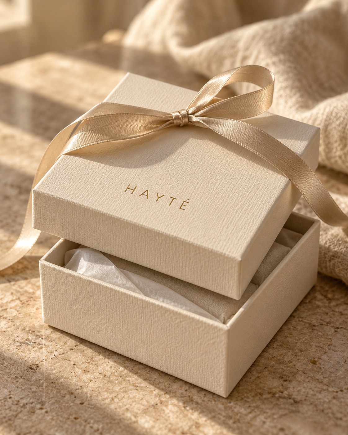 HAYTÉ ivory packaging with a champagne ribbon on softly lit linen.