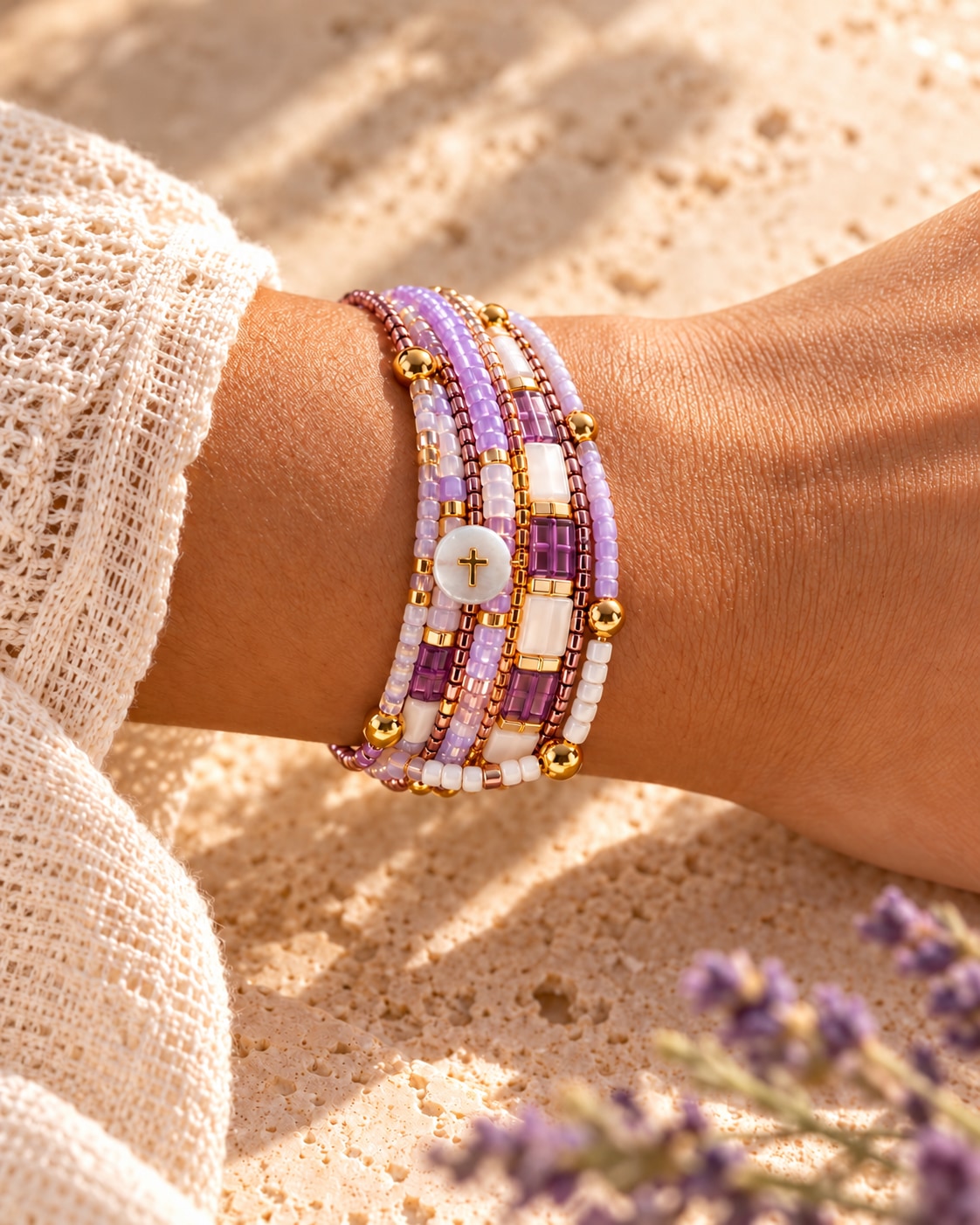 Lavender and ivory bracelets with a pearly cross detail, worn on a wrist in warm sunlight.