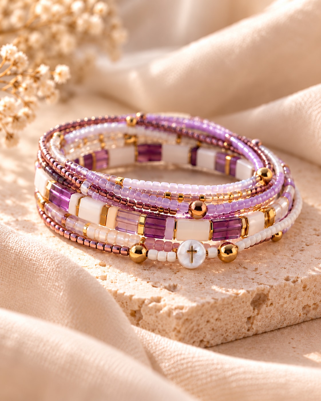 The Lavender Edit: lavender, ivory and gold-tone bracelet strands with a round white cross bead on warm stone.