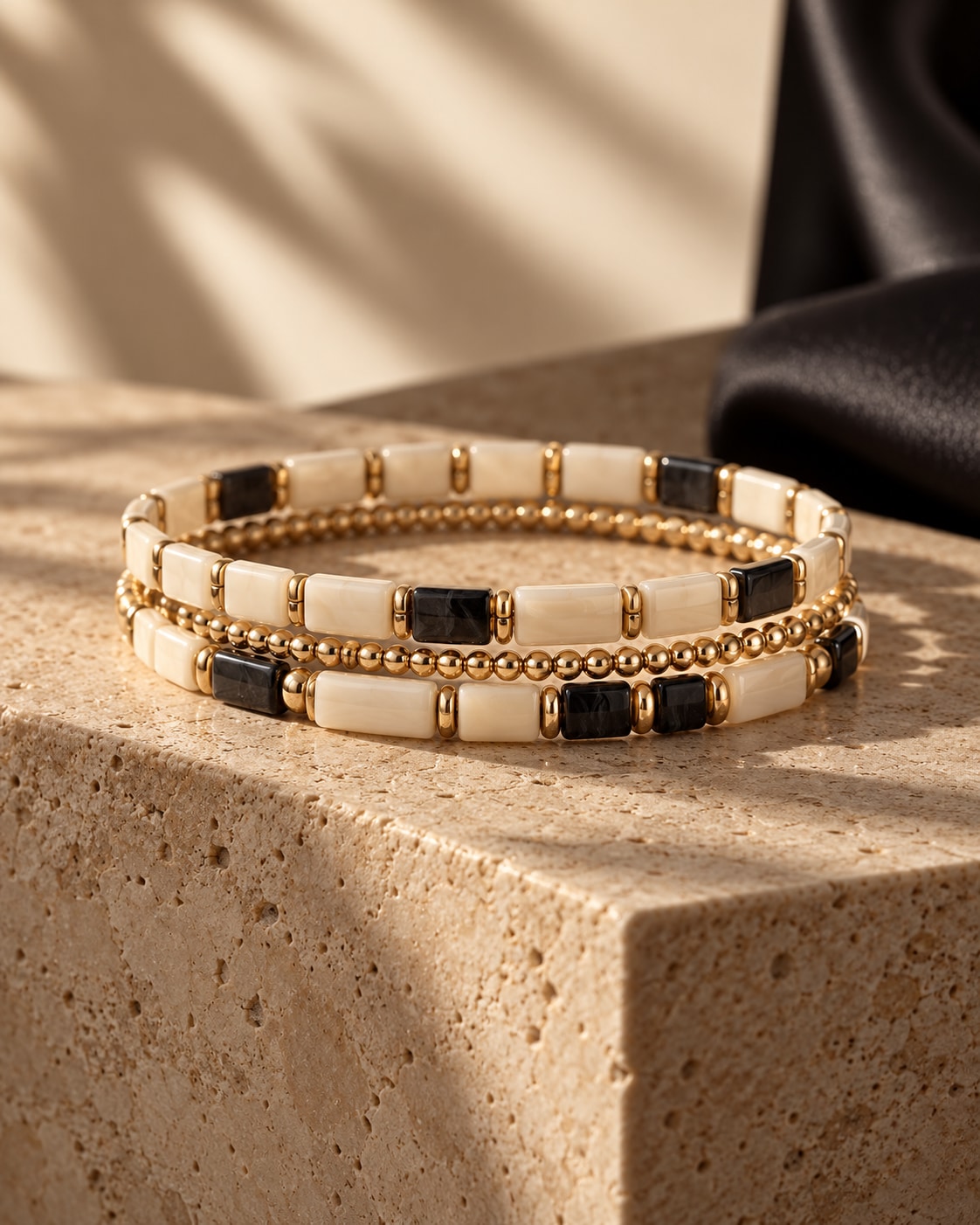 The Contrast Edit study: black, ivory and gold-tone bracelet strands against warm stone and dark fabric.